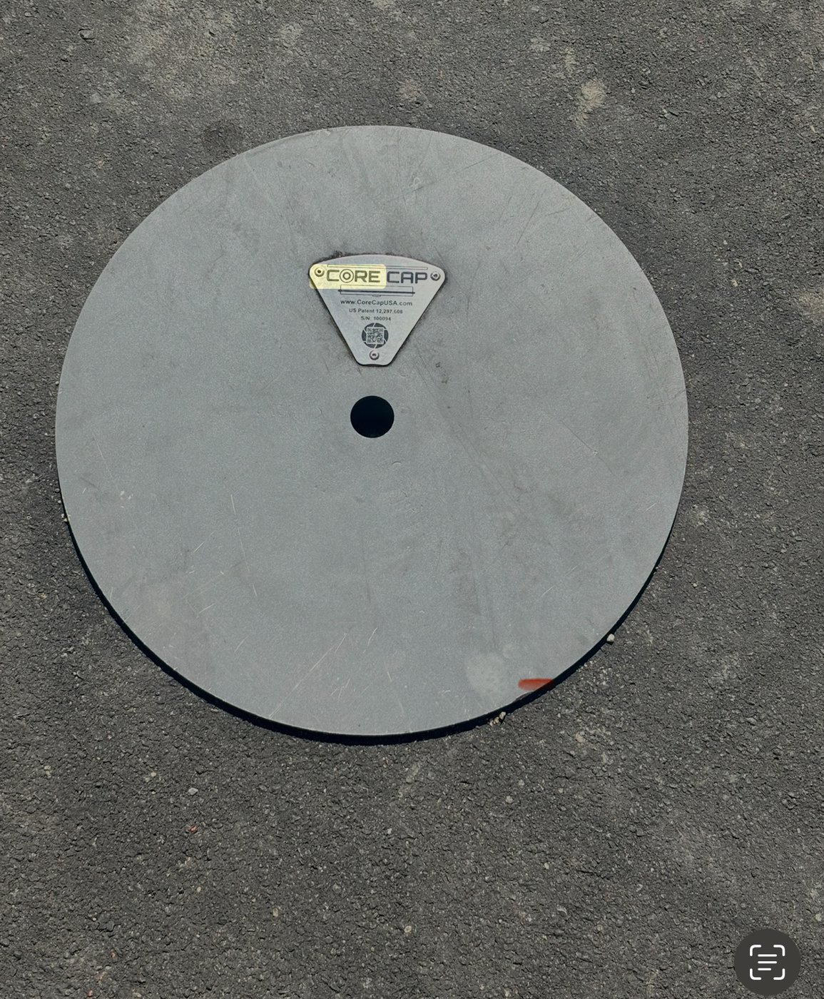 Top-down view of Core Cap installed flush in pavement, showing branded ID tag with patent number and serial number